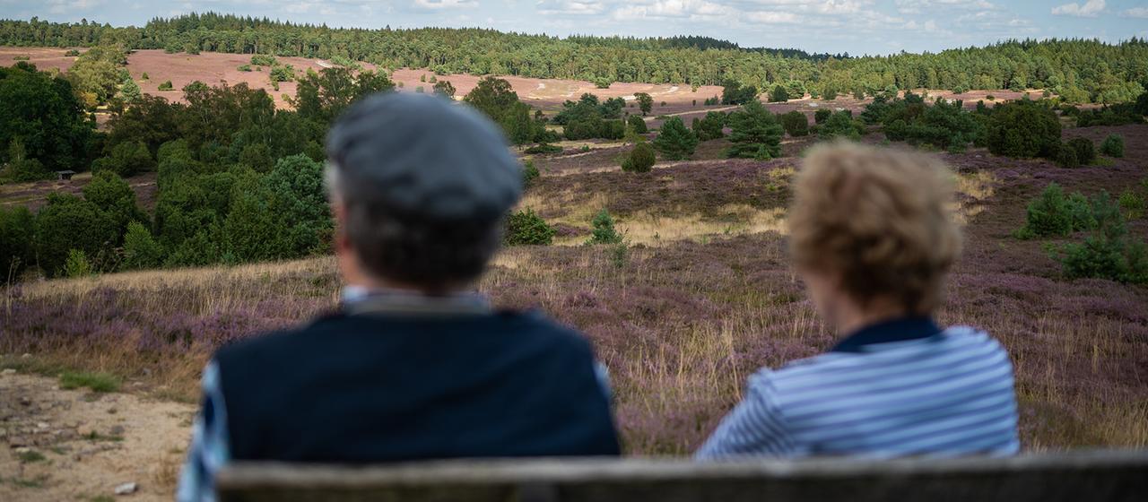 Zwei Menschen sitzen auf einer Bank in der Heidelandschaft.