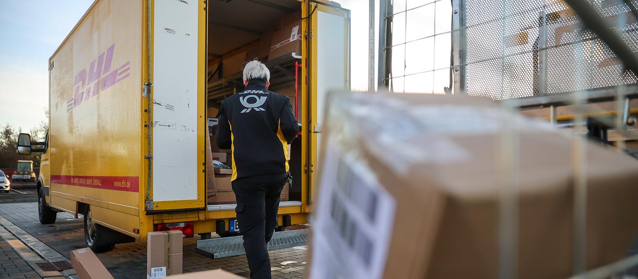 Eine Mitarbeiterin der Deutsche Post DHL belädt ihr Fahrzeug mit Päckchen und Paketen.