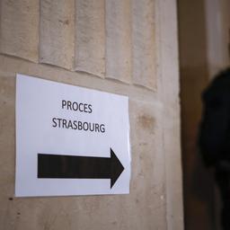 Schild, auf dem "Proces Strasbourg" steht in einem Paris Gerichtsgebäude, im Hintergrund ein Polizist