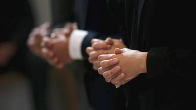 Gläubige stehen mit gefalteten Händen in der Kirche.