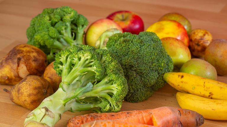 Lebensmittel auf dem Boden, darunter Brokkoli, Äpfel, Bananen und Karotten.