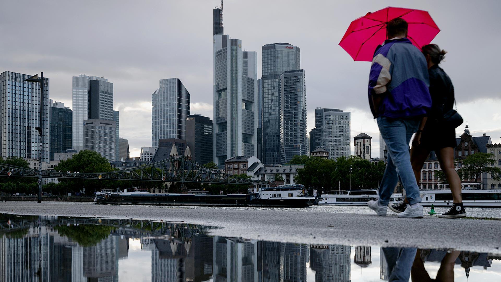 Menschen mit Regenschirm vor der Frankfurter Banken-Skyline. | picture alliance / greatif