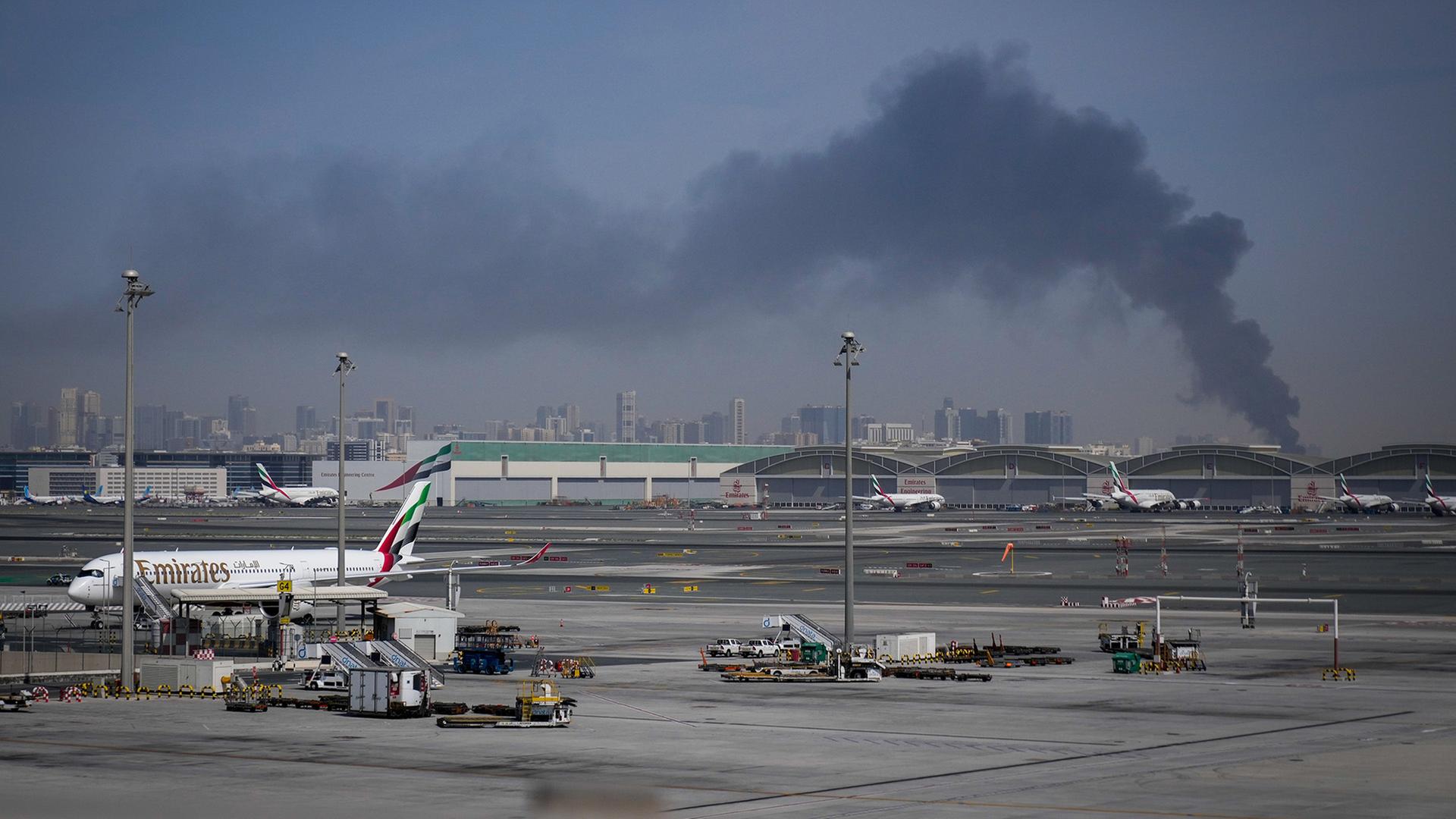 Ein Flugzeug steht auf dem Rollfeld des Flughafens Dubai, w�hrend im Hintergrund Rauch aufsteigt. | Altaf Qadri/AP/dpa
