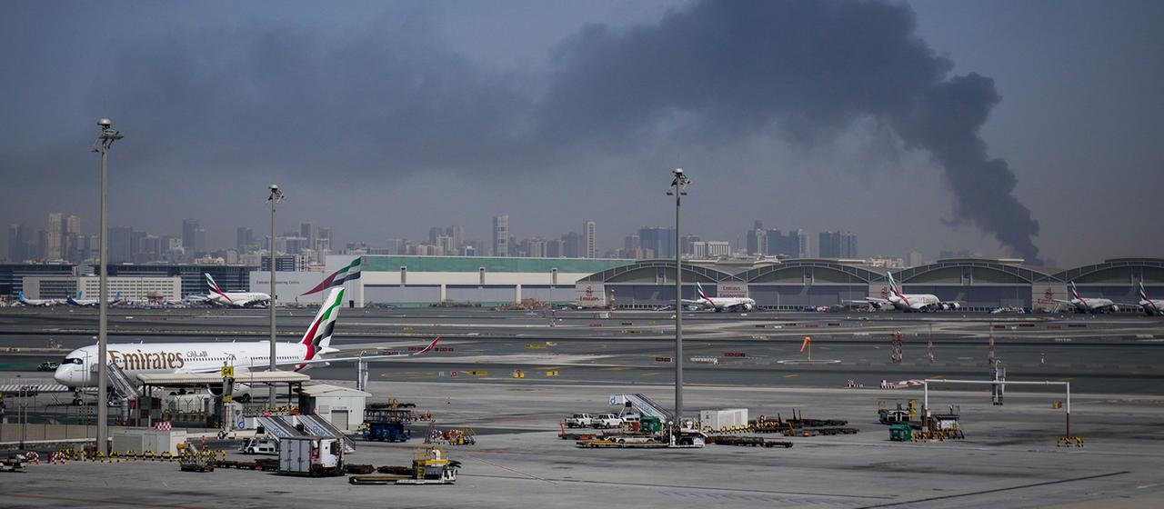 Ein Flugzeug steht auf dem Rollfeld des Flughafens Dubai, während im Hintergrund Rauch aufsteigt.