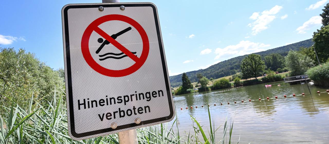 Eine Hinweistafel mit der Aufschrift "Hineinspringen verboten" ist am Ufer eines Badesees angebracht.