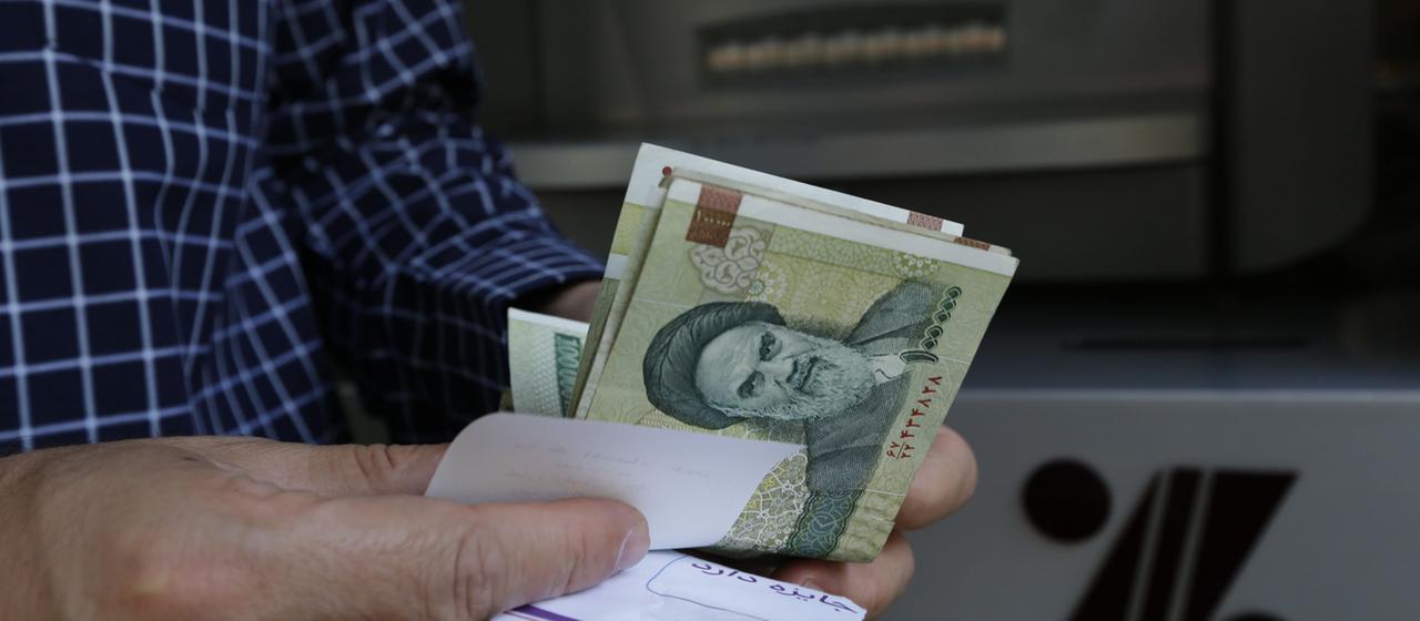 Man hält iranische Rial in der Hand