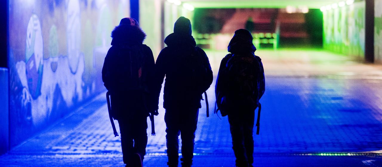 Drei Jugendliche gehen am Abend durch eine Unterführung.