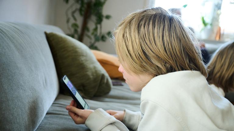  Ein Junge liegt mit dem Smartphone in der Hand auf der Couch