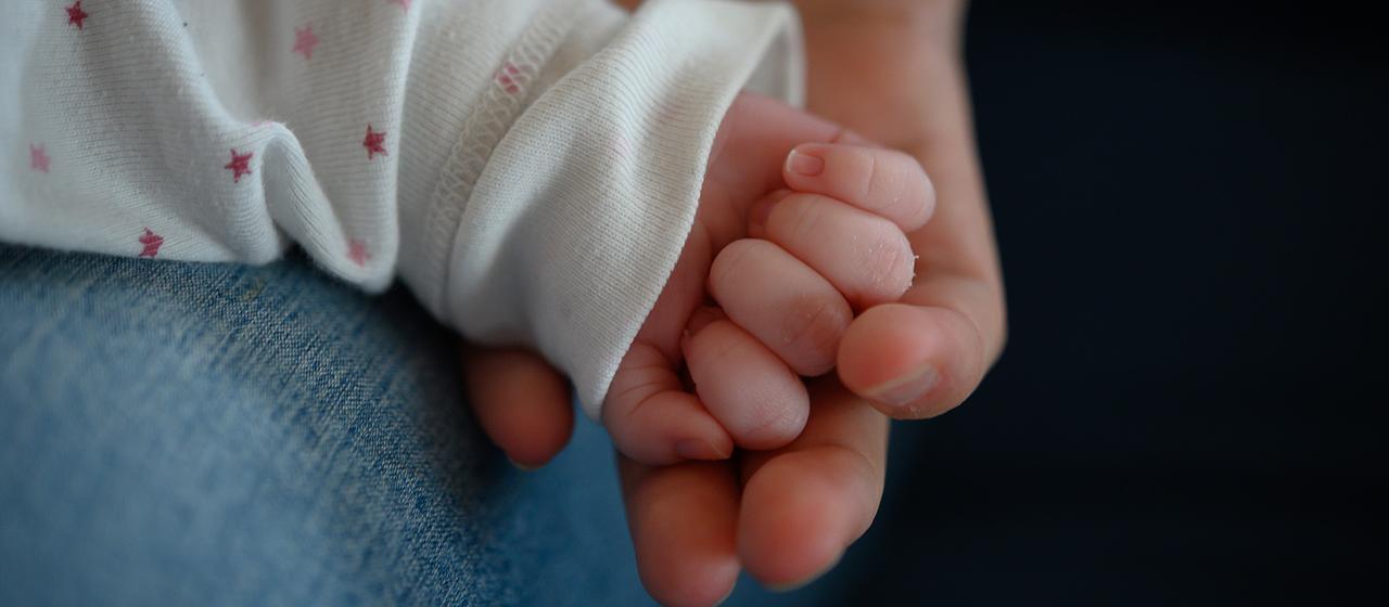 Die Hand eines Neugeborenen liegt in der Hand der Mutter
