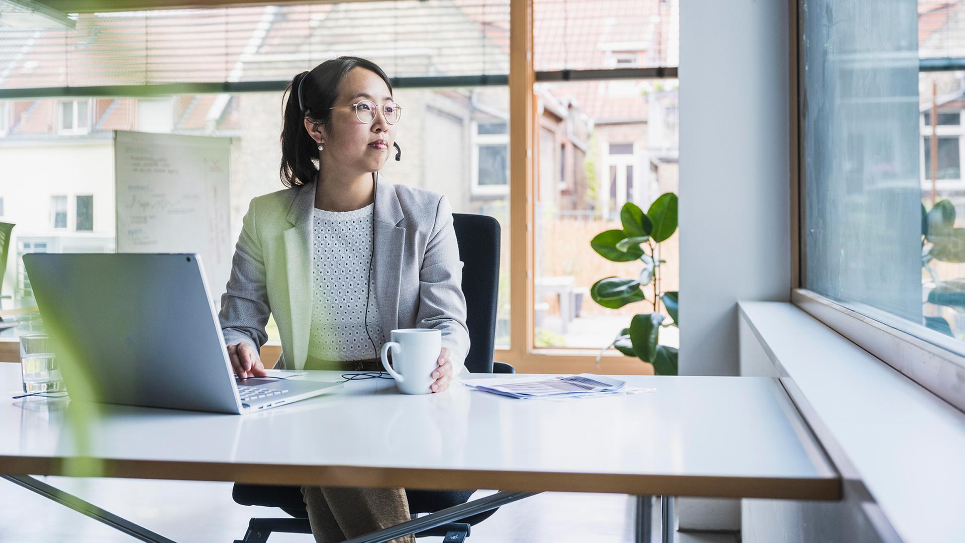 Eine Frau sitzt in einem Büro an einem Schreibtisch. | picture alliance / Westend61