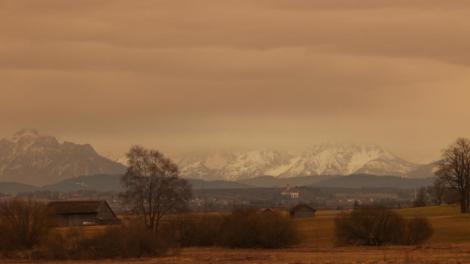 Durch Sahara-Staub orange gefärbter Himmel über Ruderatshofen im Bayern.
