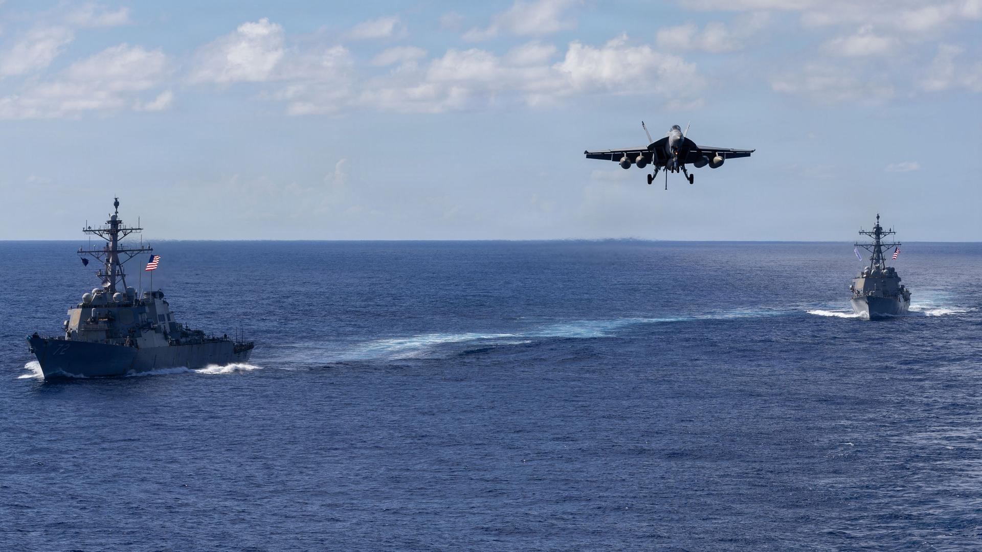 Auf diesem von der Pressestelle des Pentagons zur Verfügung gestellten Bild fahren die Lenkwaffenzerstörer der Arleigh-Burke-Klasse USS Mahan (l, DDG 72) und USS Bainbridge (DDG 96) in Formation, während ein F/A-18 Super Hornet des Carrier Air Wing Eight zur Landung auf dem Flugzeugträger USS Gerald R. Ford (CVN 78) ansetzt. | dpa