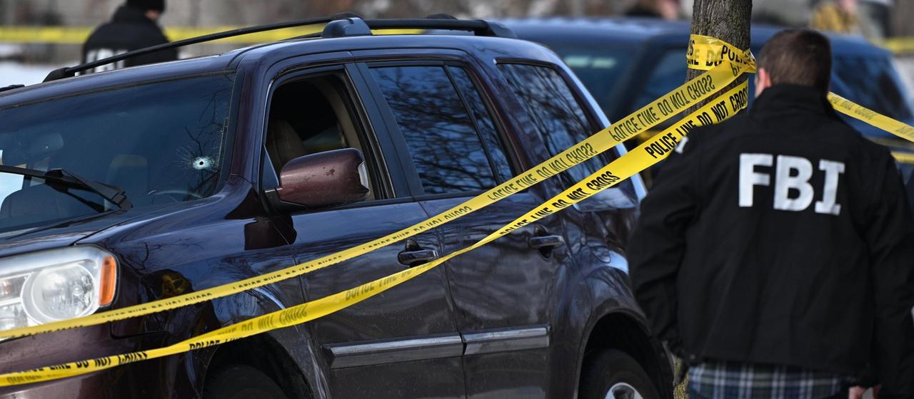 Ein Einschussloch ist in der Windschutzscheibe zu sehen, während Polizeibeamte in Minneapolis einen Tatort nach tödlichen Schüssen untersuchen.