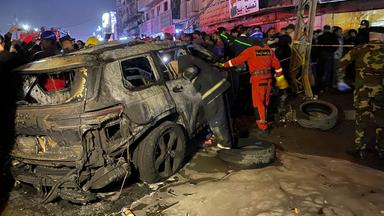 Mitglieder der Zivilverteidigung untersuchen ein verbranntes Fahrzeug.