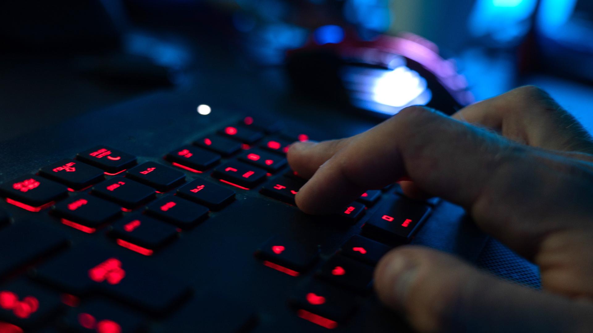 Ein Mann tippt auf einer rot beleuchteten Tastatur. | picture alliance/dpa