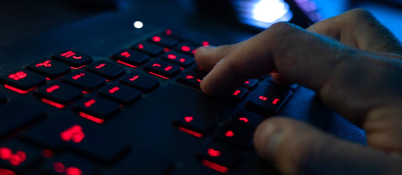 Ein Mann tippt auf einer rot beleuchteten Tastatur.