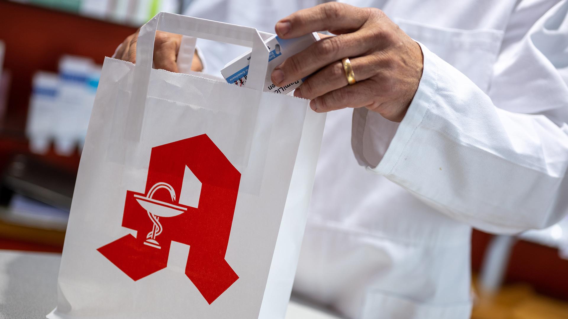 Ein Apotheker legt in einer Apotheke eine Packung mit Tabletten in eine Papiertasche mit Apotheken-Logo. | dpa