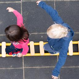 Kinder balancieren auf dem Spielplatz einer Kindertagesstätte im sächsischen Dresden auf einem Brett.
