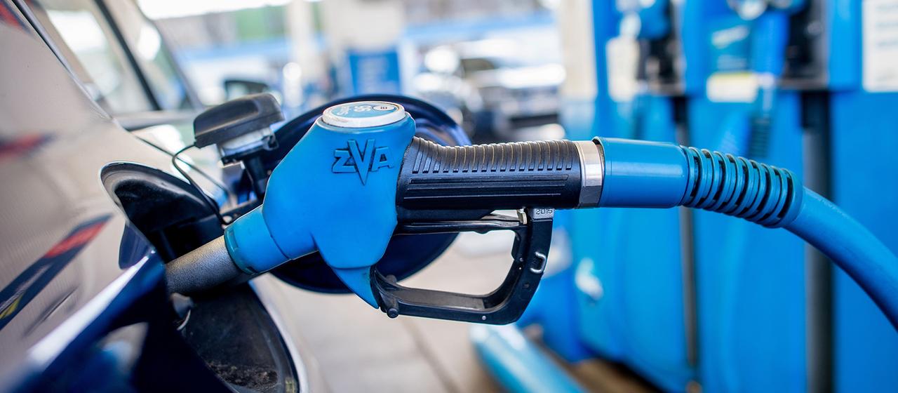 Eine Zapfpistole mit der Aufschrift "Super 95" steckt an einer Tankstelle in der Tanköffnung eines Fahrzeugs. 