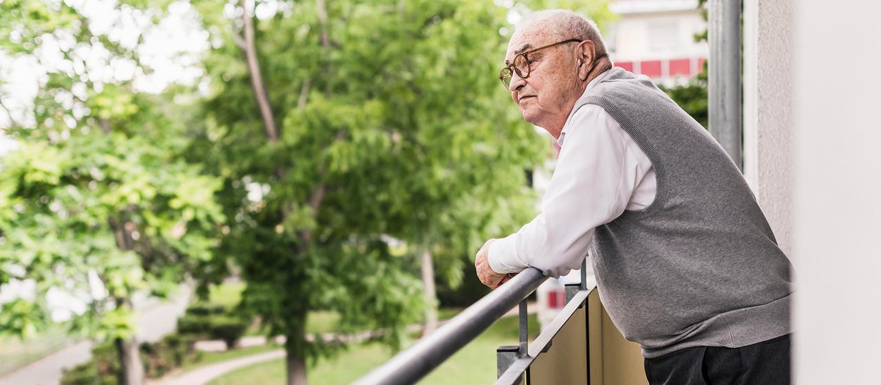 Ein älterer Mann steht auf dem Balkon.