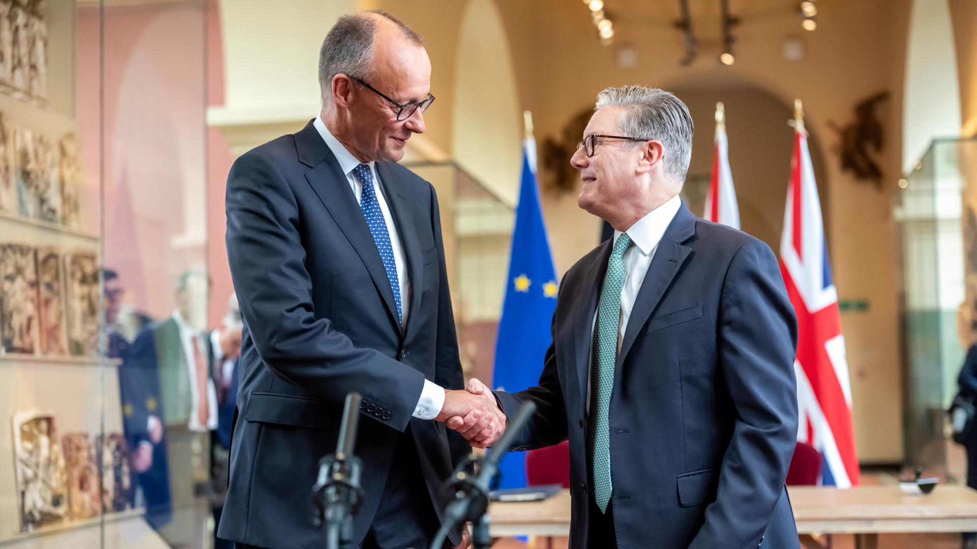Friedrich Merz und Keir Starmer schütteln sich lächelnd die Hände. | dpa