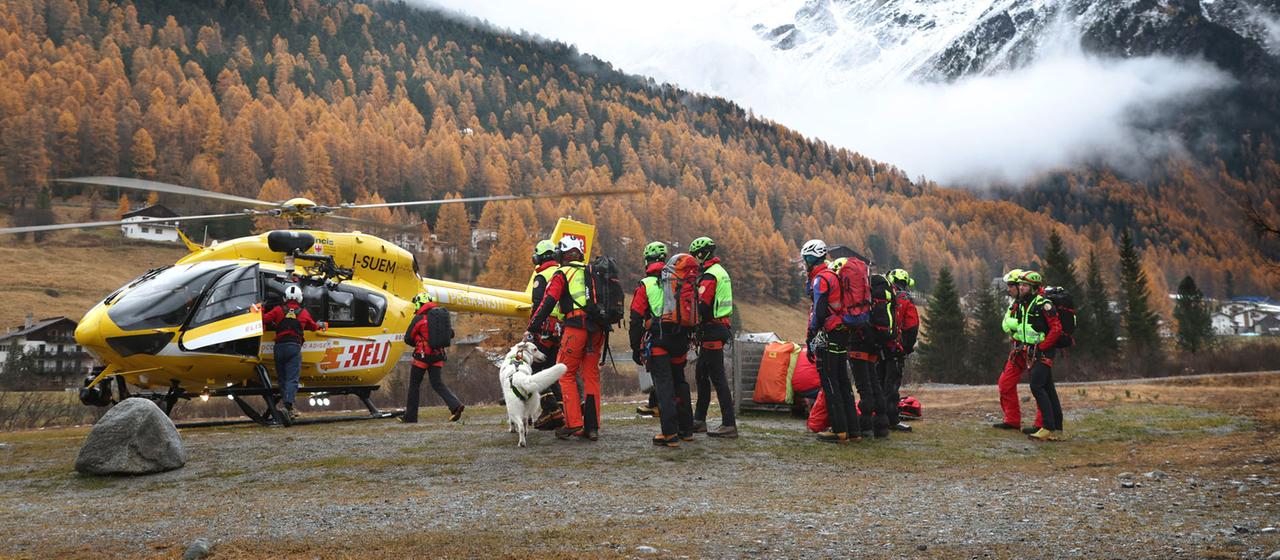 Mitglieder der Bergrettung sammeln sich vor einem Rettungshubschrauber.