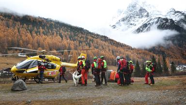 Mitglieder der Bergrettung sammeln sich vor einem Rettungshubschrauber.