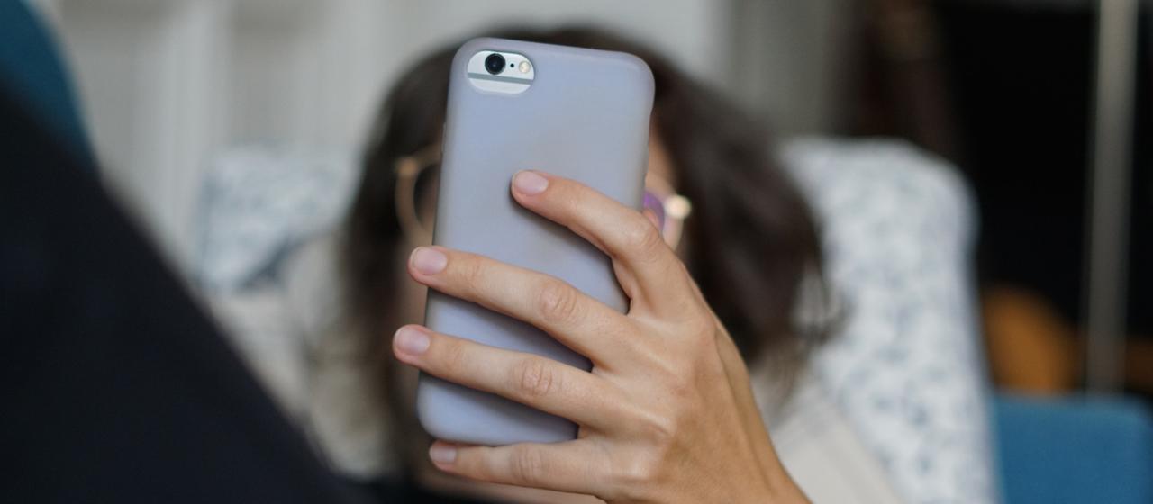 A woman lies on a sofa and uses her cell phone.