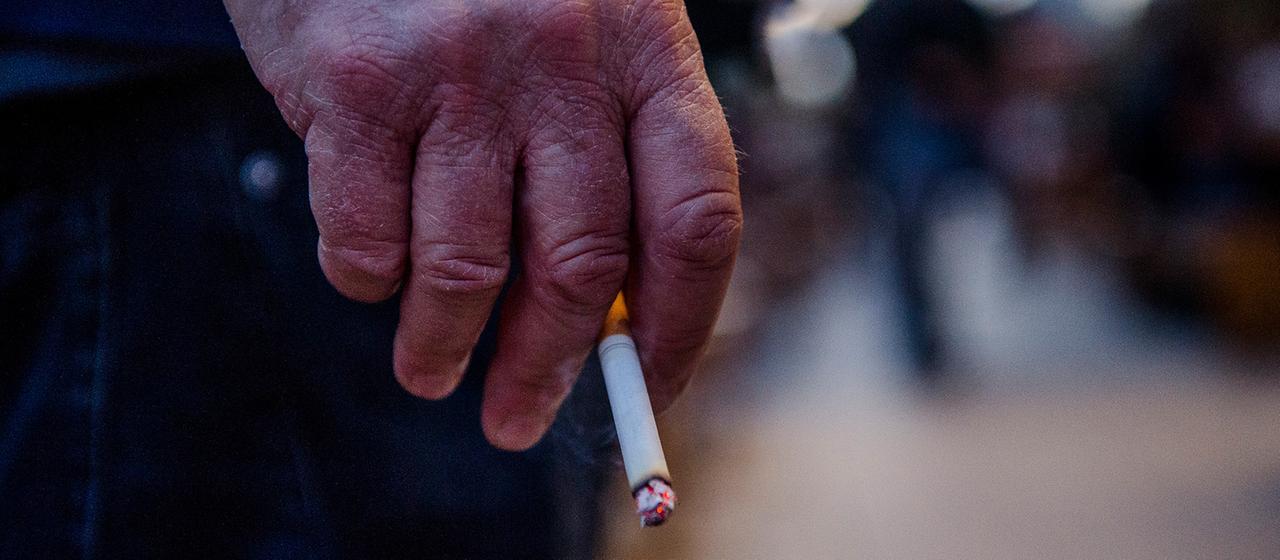 Ein Mann steht auf einer Straße und hält eine Zigarette in seiner Hand.