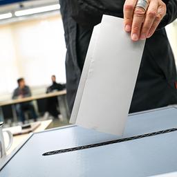 Eine Wählerin wirft ihren Sitmmzettel in eine Wahlurne, neben der ein Becher steht, auf dem die Bremer Stadtmusikanten abgebildet sind.