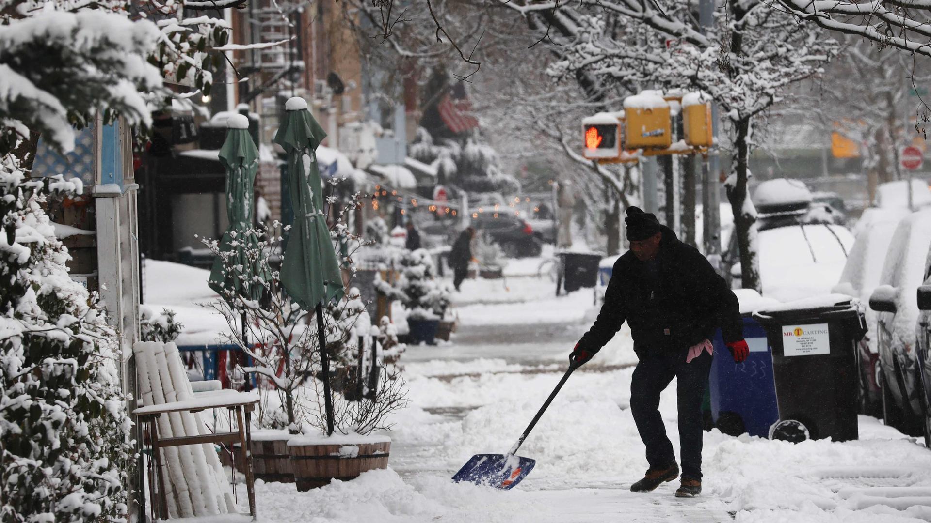 Ein Mann schippt Schnee auf einem Gehweg in Brooklyn. | Getty Images via AFP