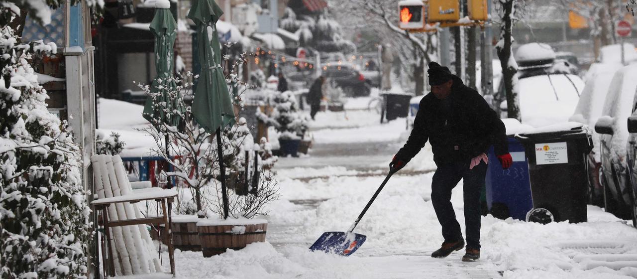 A man shovels snow on a sidewalk in Brooklyn.