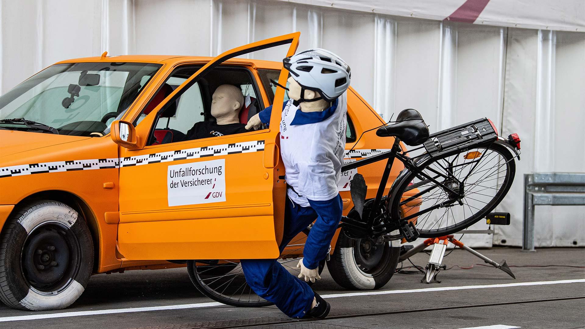 Crashtest-Dummy mit Fahrrad fährt gegen die geöffnete Tür eines geparkten Autos. | picture alliance/dpa