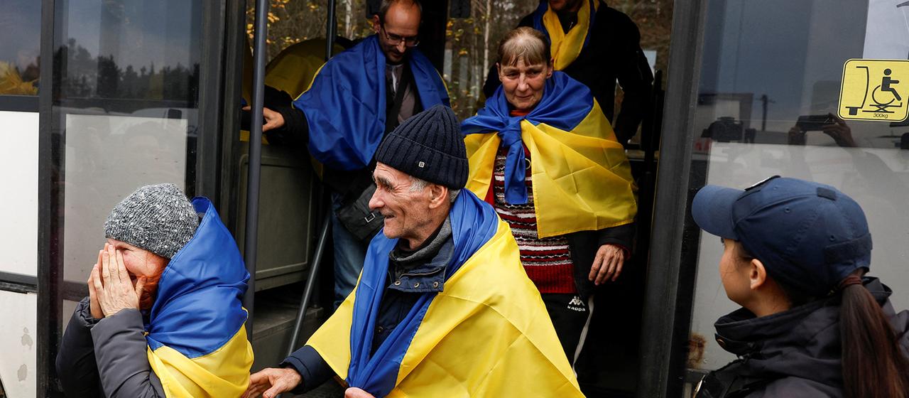 Mehrere Menschen, in ukrainische Flaggen gehüllt, steigen aus einem Bus.