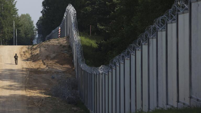 Ein polnischer Grenzschützer patrouilliert an einer Metallmauer an der Grenze zwischen Polen und Belarus. (Aufnahme vom 30. Juni 2022)