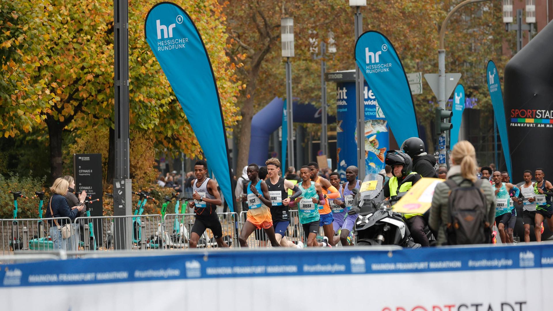 Foto: Marathonläufer umgeben von Zuschauenden hinter Absperrungen. Zwischendrin blaue Fahnen mit dem hr-Logo. | imago
