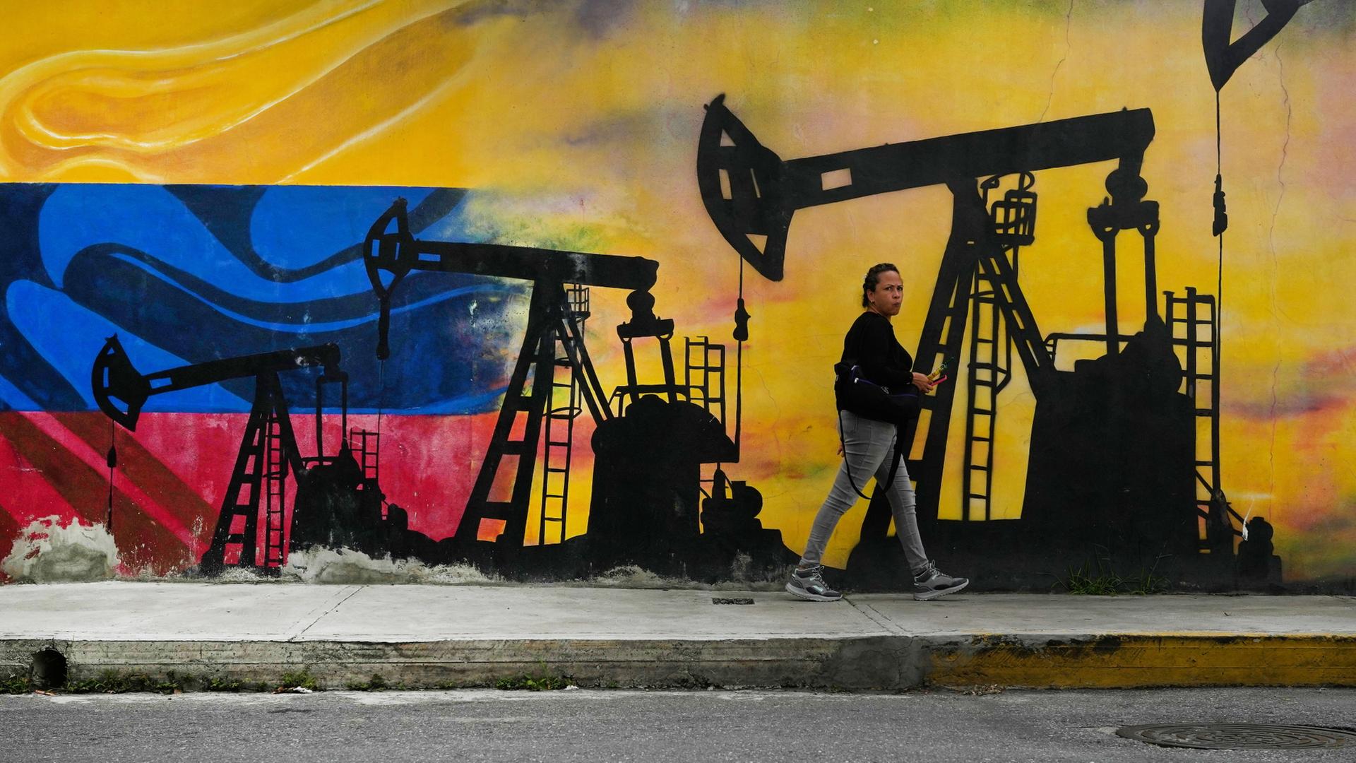Ein Mann läuft an einer Mauer mit einem Graffiti vorbei, darauf Ölpumpen. | dpa