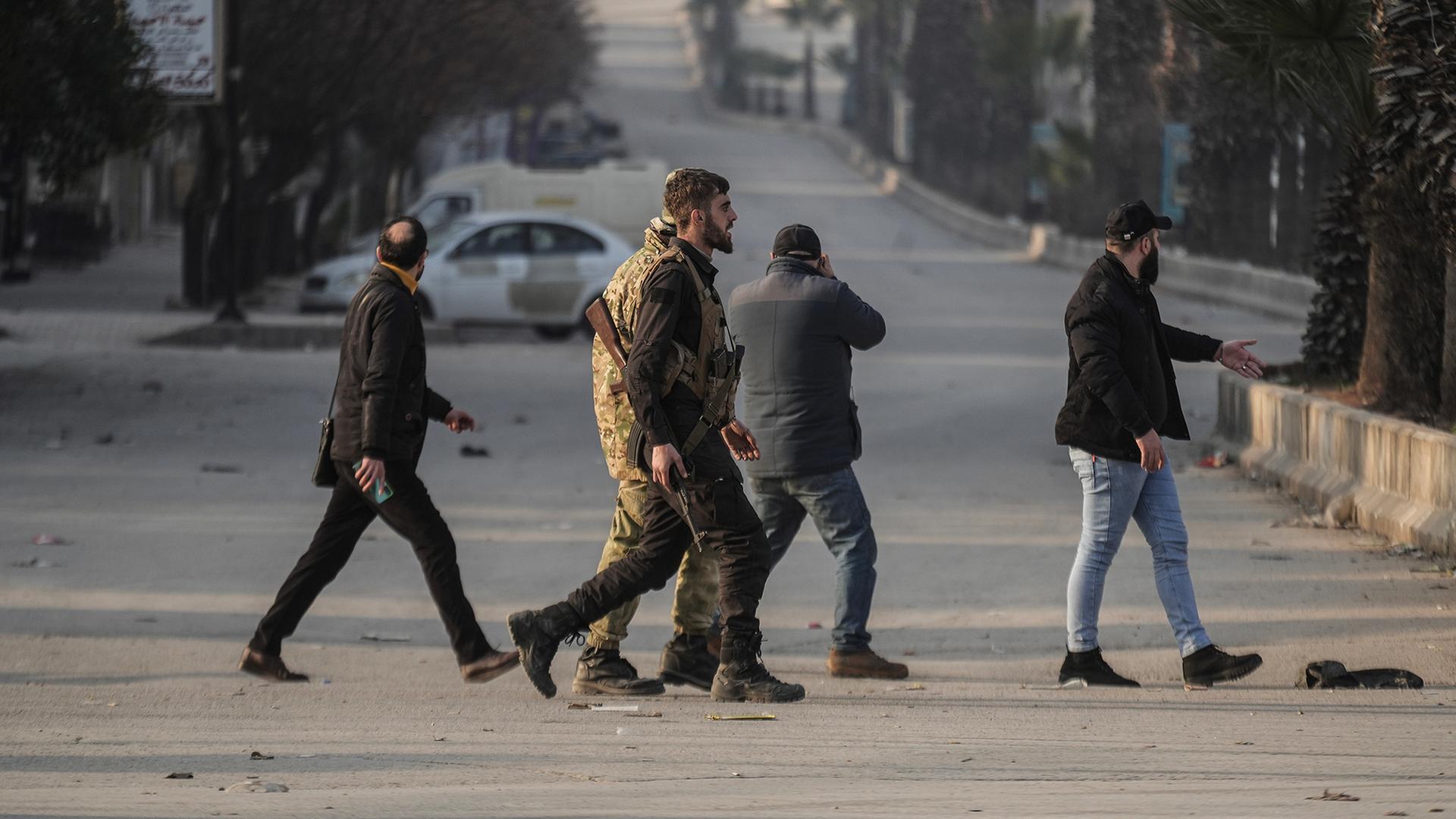Teilweise bewaffnete und uniformierte Männer überqueren eine Straße. | dpa