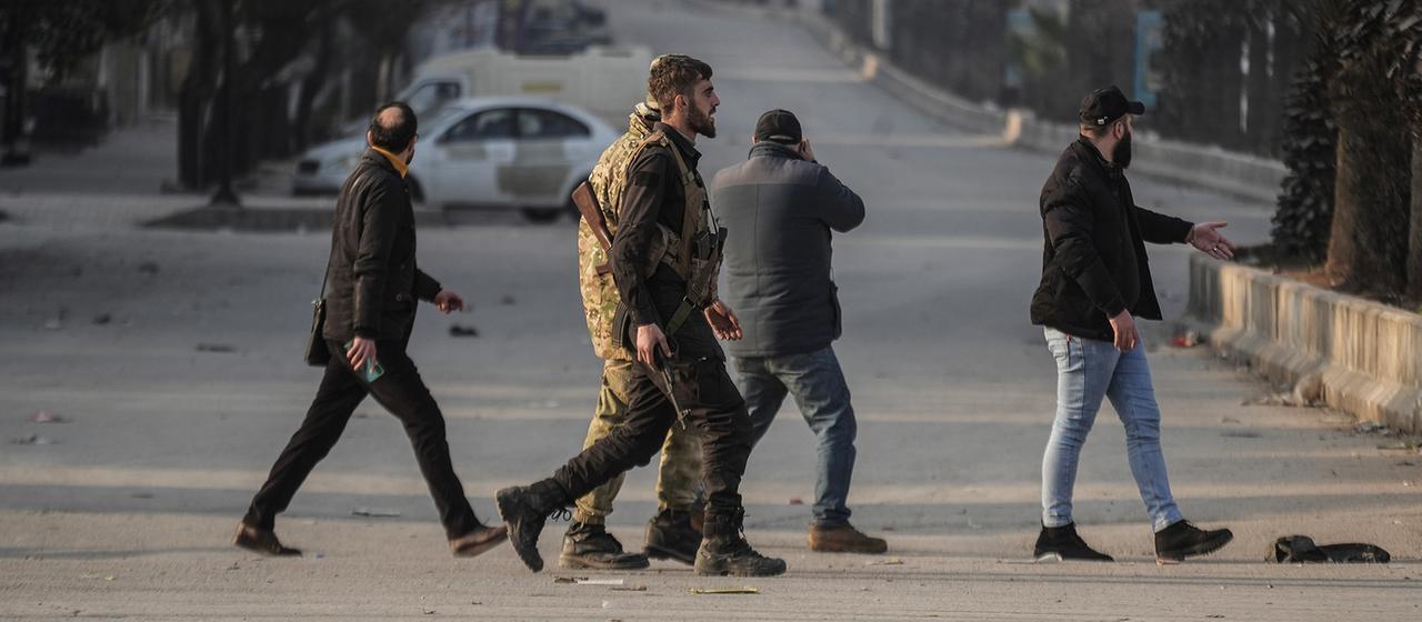 Teilweise bewaffnete und uniformierte Männer überqueren eine Straße.