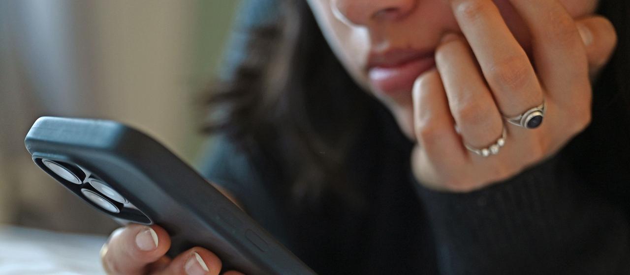 Eine junge Frau sieht auf das Display eines Smartphones.