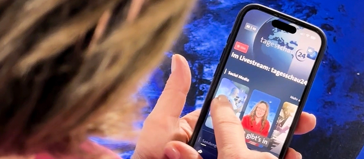 Susanne Daubner steht im Studio und schaut auf die tagesschau-App.