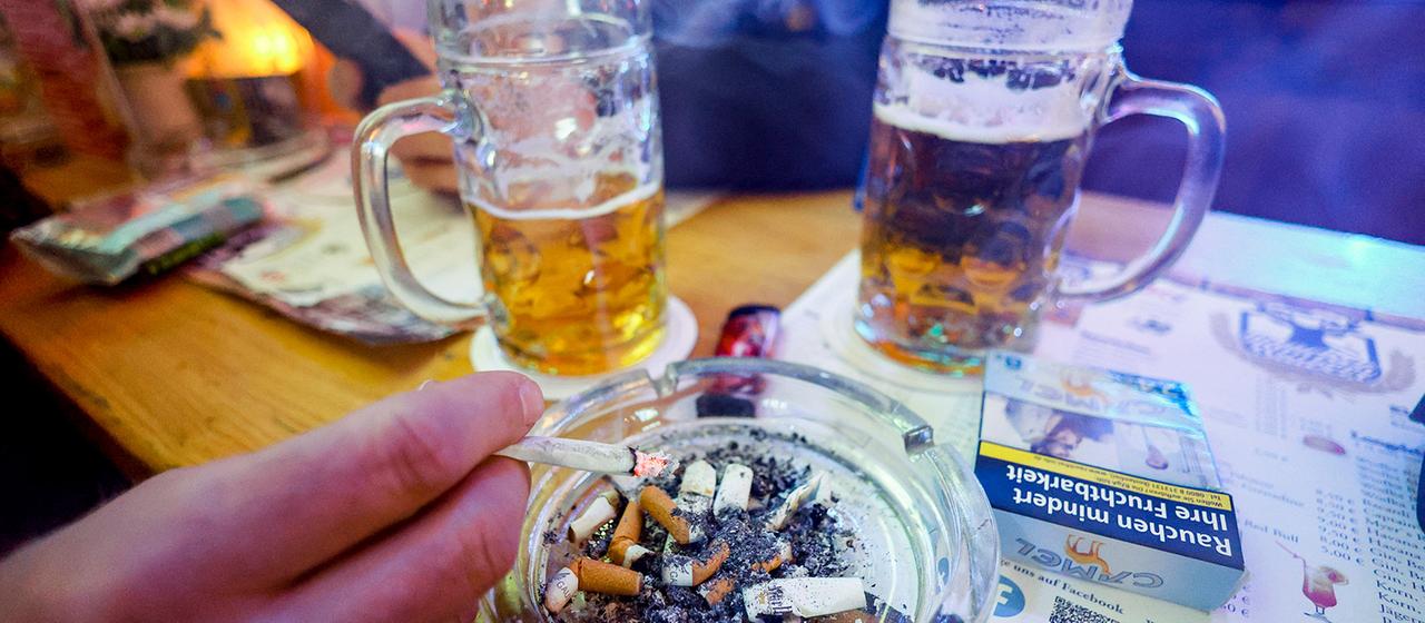 Ein Mann ascht in einer Rauchkneipe seine Zigarette ab. 